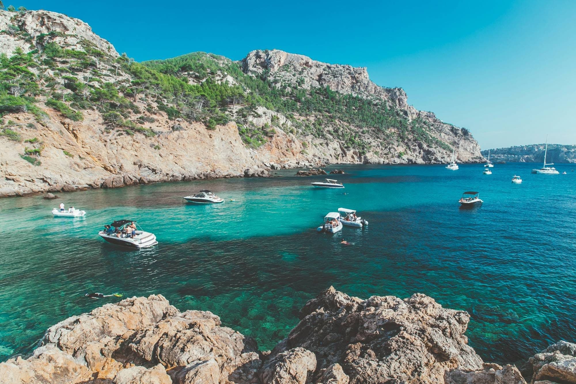Turquoise cove with boats at anchor beneath the pine-covered cliffs of Majorca's north-west coast